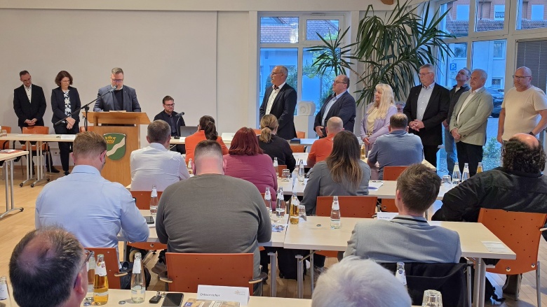 Sitzungsraum der Gemeindevertretung Flieden mit Personen an Tischen. Im Hintergrund Bürgermeister am Rednerpult. Auf der rechten Seite stehen sechs neu gewählte Beigeordnete.